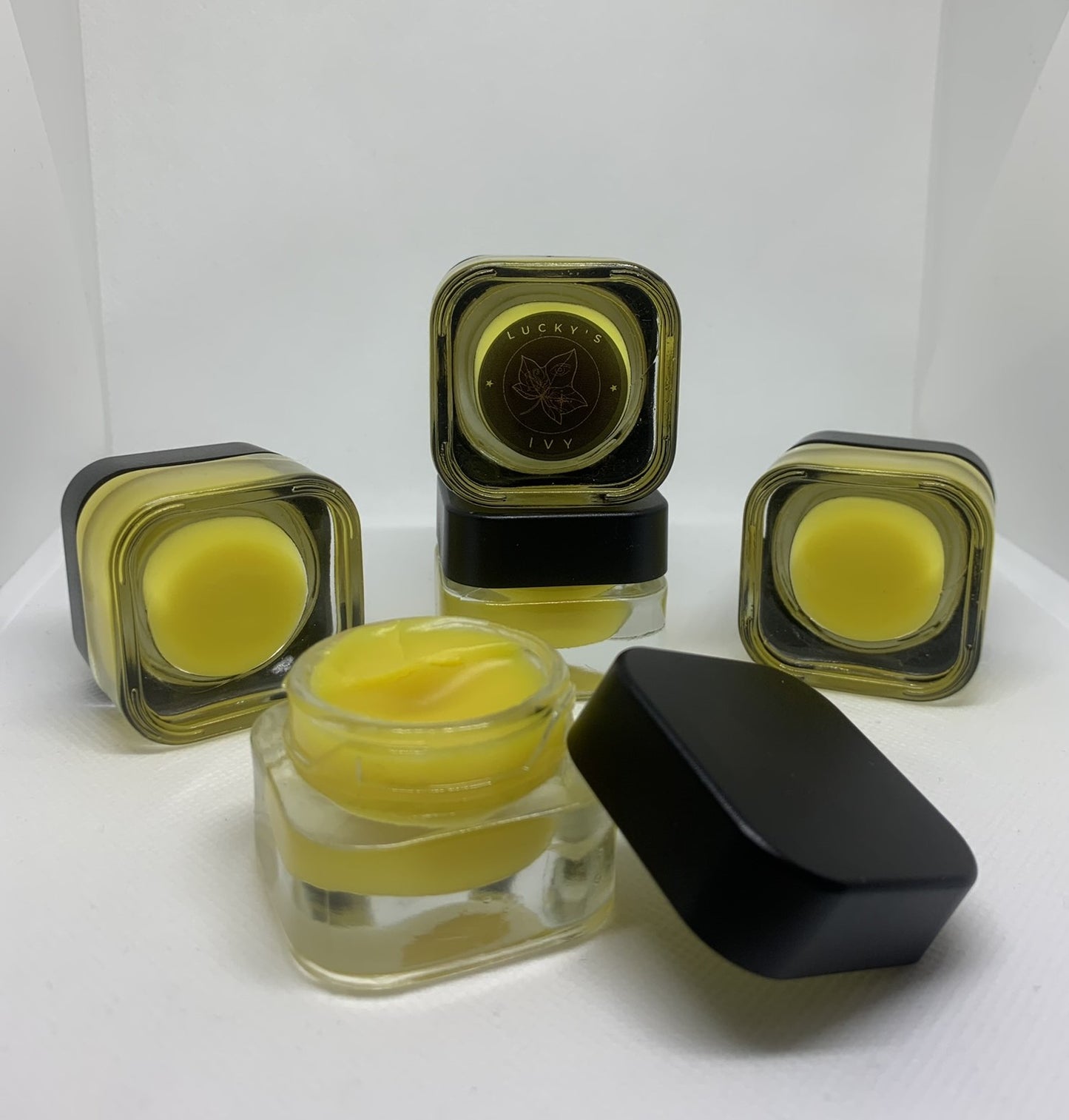 Image of Lucky's Ivy Golden Night Under-Eye Balm. One jar is open to show product texture, other jars are closed showing the outside of the product.