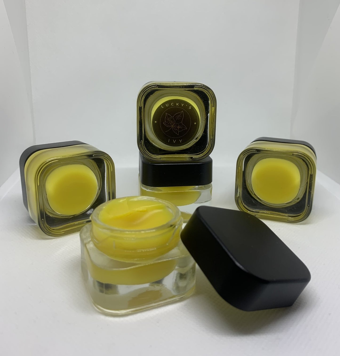 Image of Lucky's Ivy Golden Night Under-Eye Balm. One jar is open to show product texture, other jars are closed showing the outside of the product. 