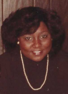 Image of Ivy wearing a black turtleneck and pearls, smiling, with thick, straight but curled hair.